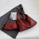Elegante rote Ledertasche mit passender Clutch auf grauem Stoff. Perfekt für stilvolle Damenmode und Accessoires. Hochwertige Handtasche.