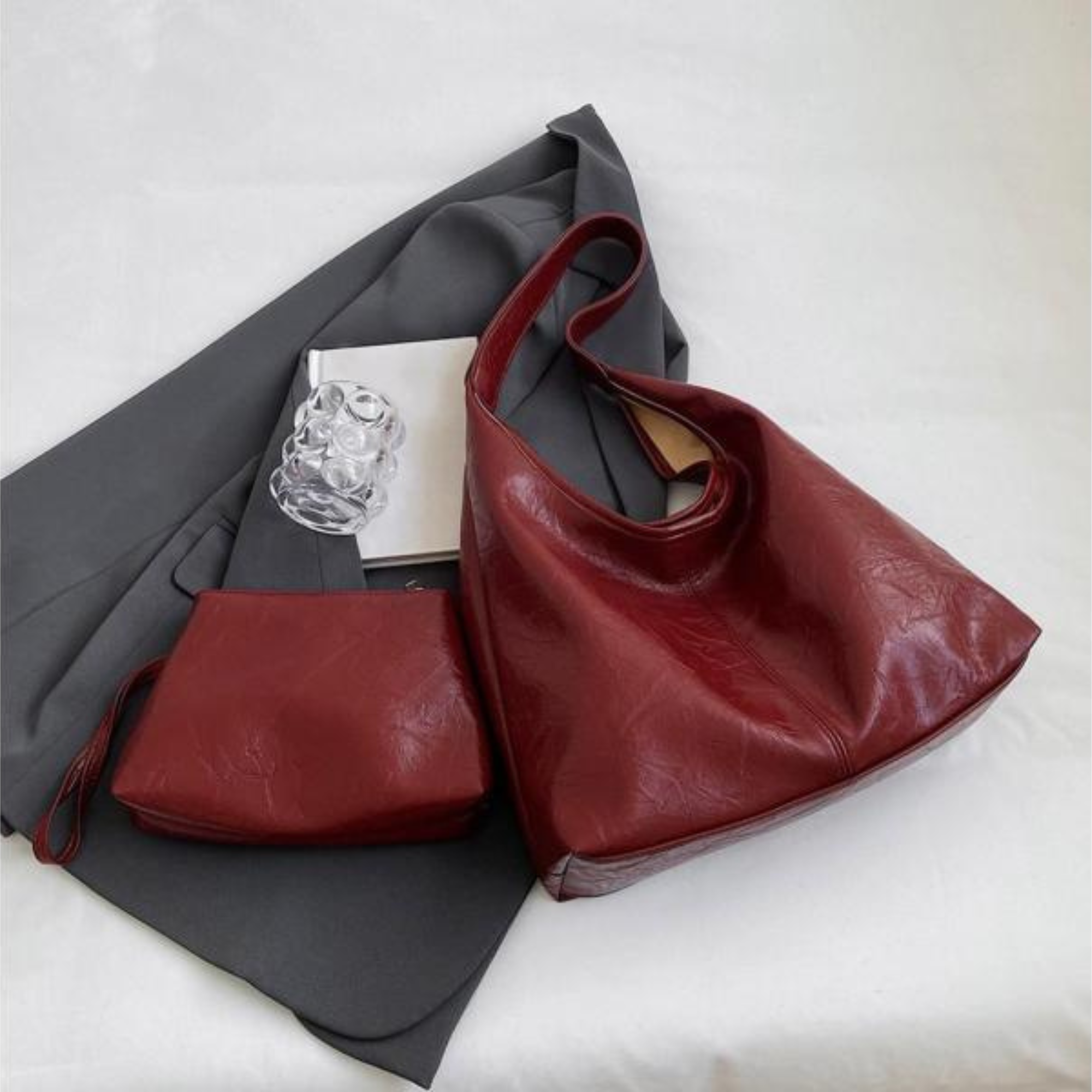 Elegante rote Ledertasche mit passender Clutch auf grauem Stoff. Perfekt für stilvolle Damenmode und Accessoires. Hochwertige Handtasche.