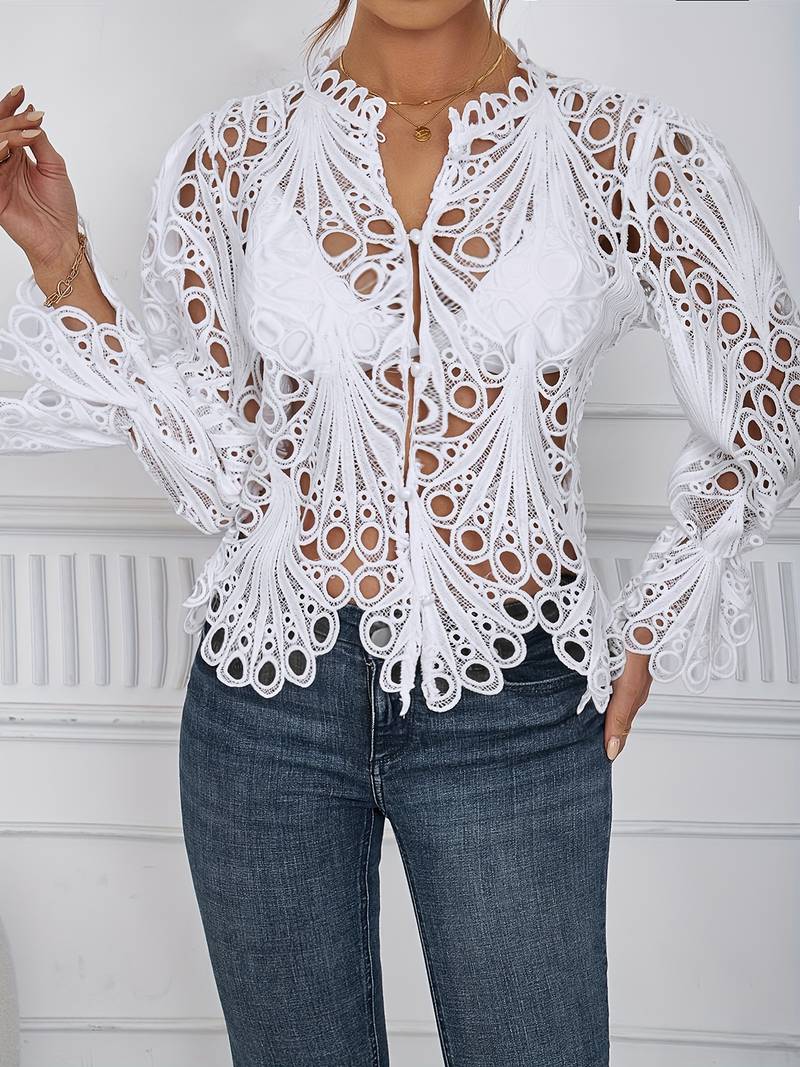 Elegante weiße Spitzenbluse mit aufwendigem Lochmuster, kombiniert mit dunkelblauer Jeans. Perfekt für stilvolle, modische Outfits.