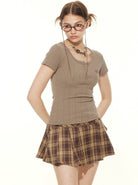 Frau in modischem Outfit: braunes T-Shirt, karierter Rock. Trendige Brille, lässige Frisur. Perfekt für urbanen, jugendlichen Stil.