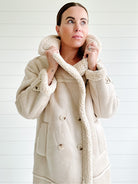 Frau in beigem Lammfellmantel mit Kapuze, elegantes Winteroutfit, modischer Damenmantel, warme Oberbekleidung, stilvolle Wintermode.