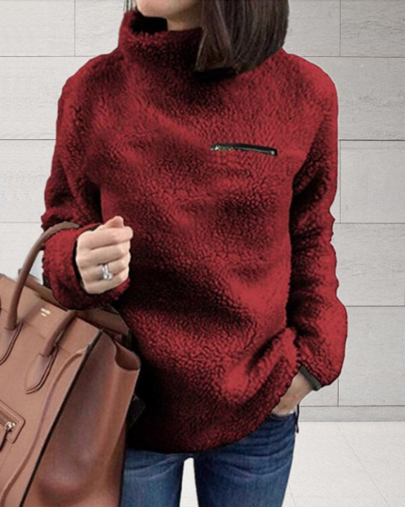 Damenmode: Roter Teddy-Fleece-Pullover mit hohem Kragen und Reißverschlusstasche, kombiniert mit brauner Handtasche. Wintermode, kuschelig, stylisch.