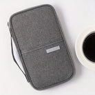 Graue Reise-Passhülle aus Stoff neben einer Tasse Kaffee auf weißem Hintergrund.