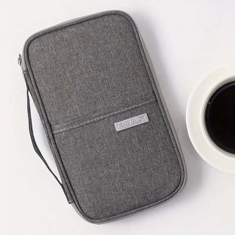 Graue Reise-Passhülle aus Stoff neben einer Tasse Kaffee auf weißem Hintergrund.