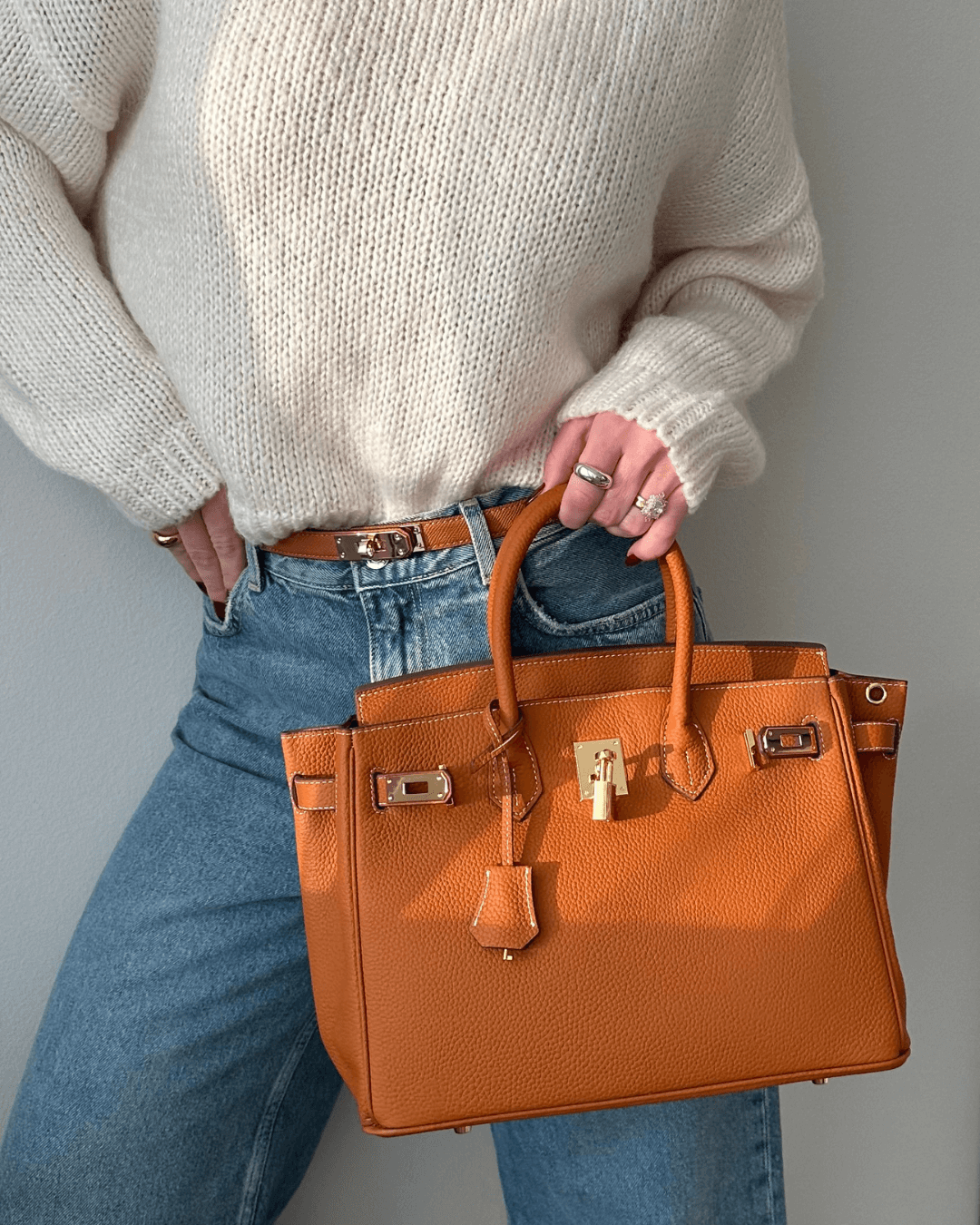 Frau mit brauner Lederhandtasche, Strickpullover und Jeans, modisches Accessoire, Damenmode.