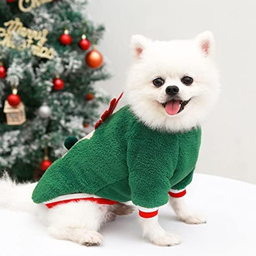 Weißer Pomeranian im grünen Weihnachtskostüm vor geschmücktem Weihnachtsbaum. Niedlicher Hund, festliche Kleidung, Weihnachtsdekoration.