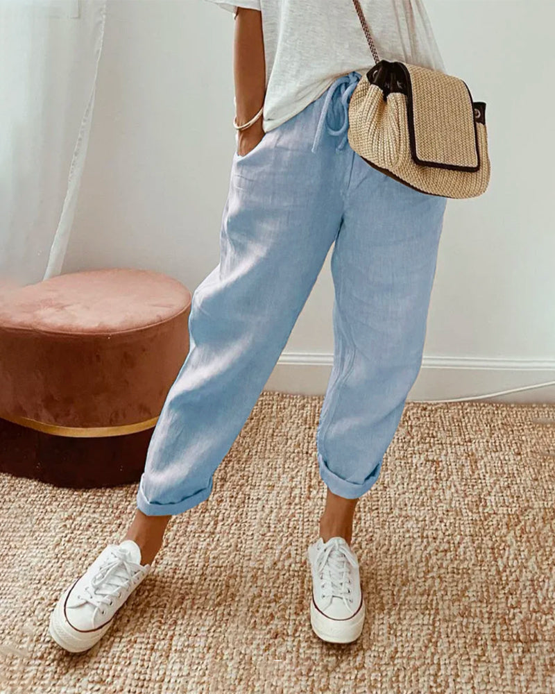 Damenmode: Lässige Leinenhose in Hellblau, kombiniert mit weißen Sneakers und Strohtasche. Perfekt für Sommer und Freizeit.