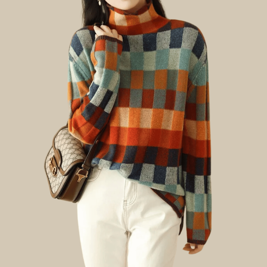 Damenpullover mit Karomuster in Blau, Orange und Grün, kombiniert mit weißer Hose und brauner Umhängetasche. Modetrend Herbst/Winter.