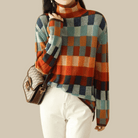 Damenpullover mit Karomuster in Blau, Orange und Grün, kombiniert mit weißer Hose und brauner Umhängetasche. Modetrend Herbst/Winter.