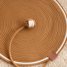 Katzenspielzeug Kratzmatte aus braunem Seil, rund, mit weißem Rand und Ledertag.