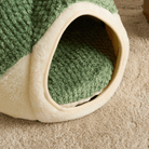 Grünes Katzenbett aus Plüsch, gemütlich, Höhlenform, ideal für Haustiere, auf Teppich.