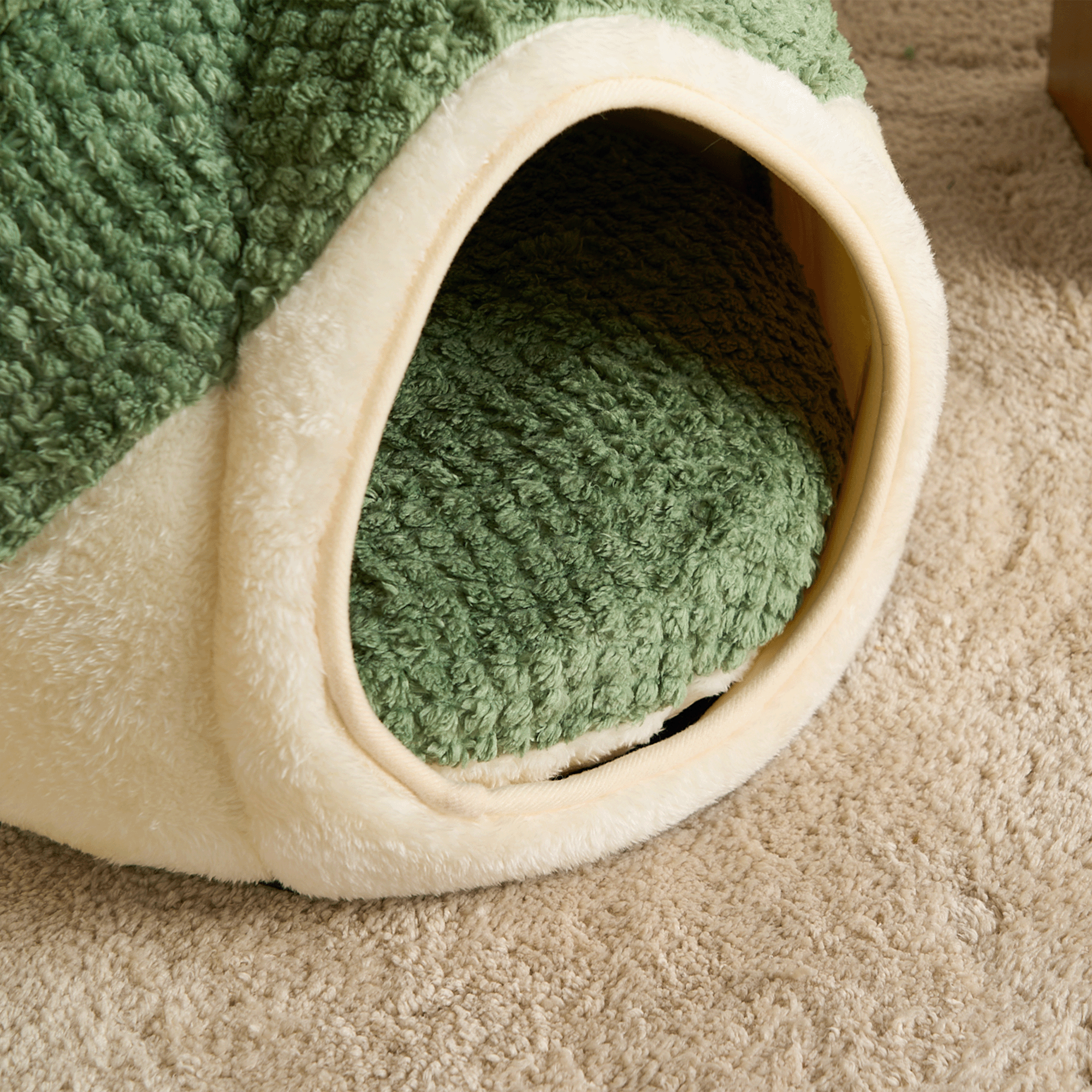 Grünes Katzenbett aus Plüsch, gemütlich, Höhlenform, ideal für Haustiere, auf Teppich.