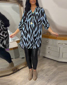 Damenmode: Lässige Tunika mit blau-schwarzem Muster, kombiniert mit schwarzen Leggings und Stiefeletten. Perfekt für stilvolle Freizeitlooks.