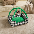 Schwarz-weiß kariertes Katzenbett mit grünem Spielbogen und hängendem Spielzeug auf Teppich.