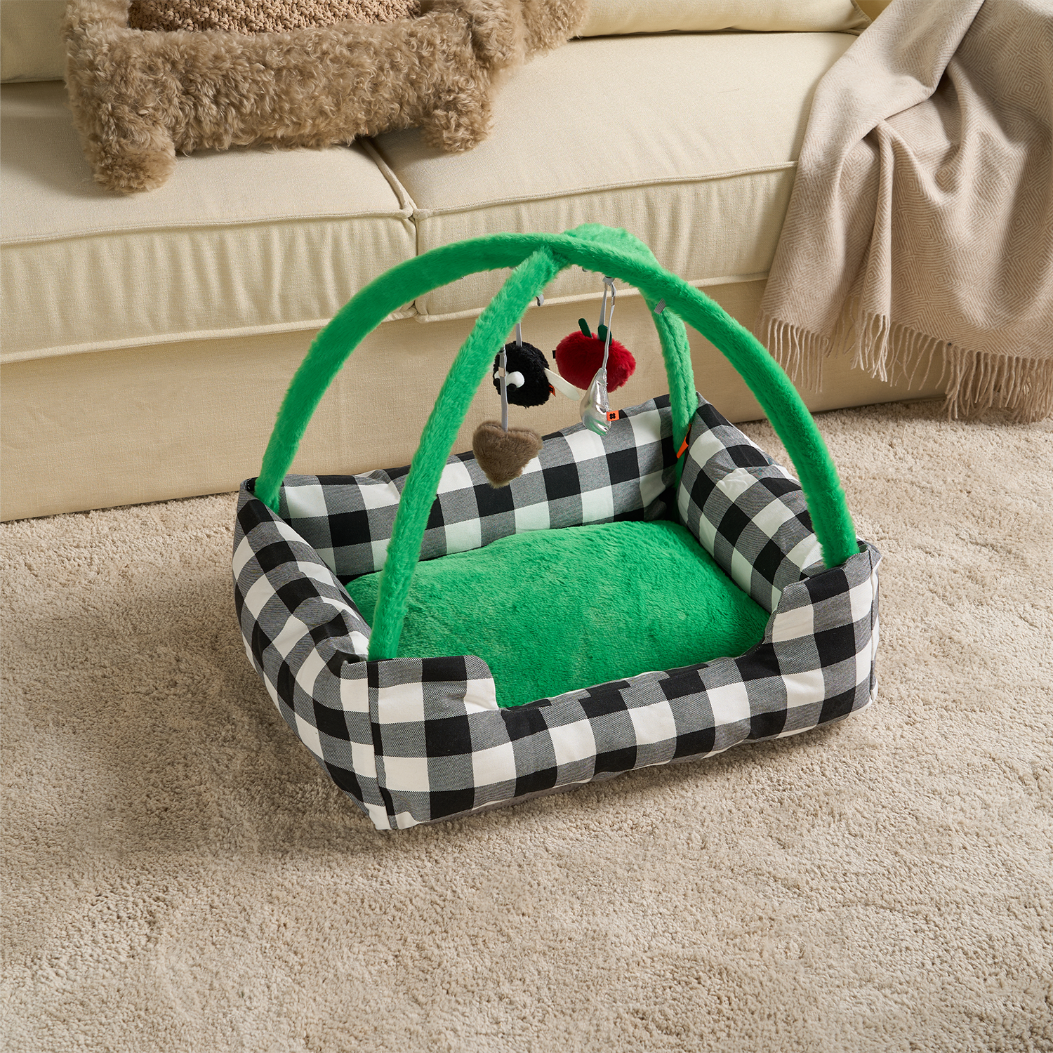 Schwarz-weiß kariertes Katzenbett mit grünem Spielbogen und hängendem Spielzeug auf Teppich.