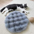 Graues, weiches, rundes Haustier-Schlafkissen auf Teppich mit schlafender Katze.