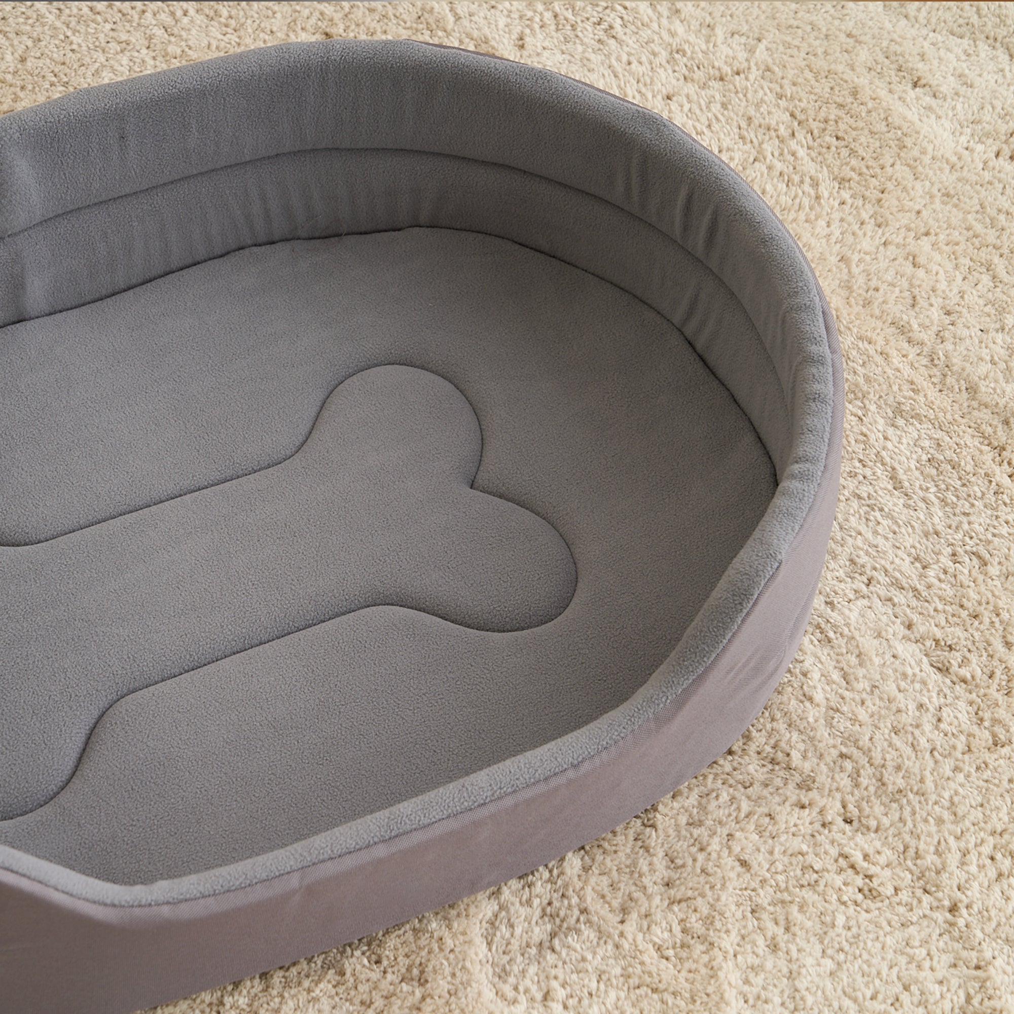 Graues Hundebett aus Plüsch, oval, auf beigem Teppich, ideal für Haustiere, gemütlich und weich.
