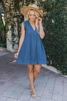 Frau in blauem Sommerkleid und Strohhut, steht auf gepflastertem Weg vor grüner Hecke. Modetrend, Sommeroutfit, Damenmode, Freizeitkleidung.
