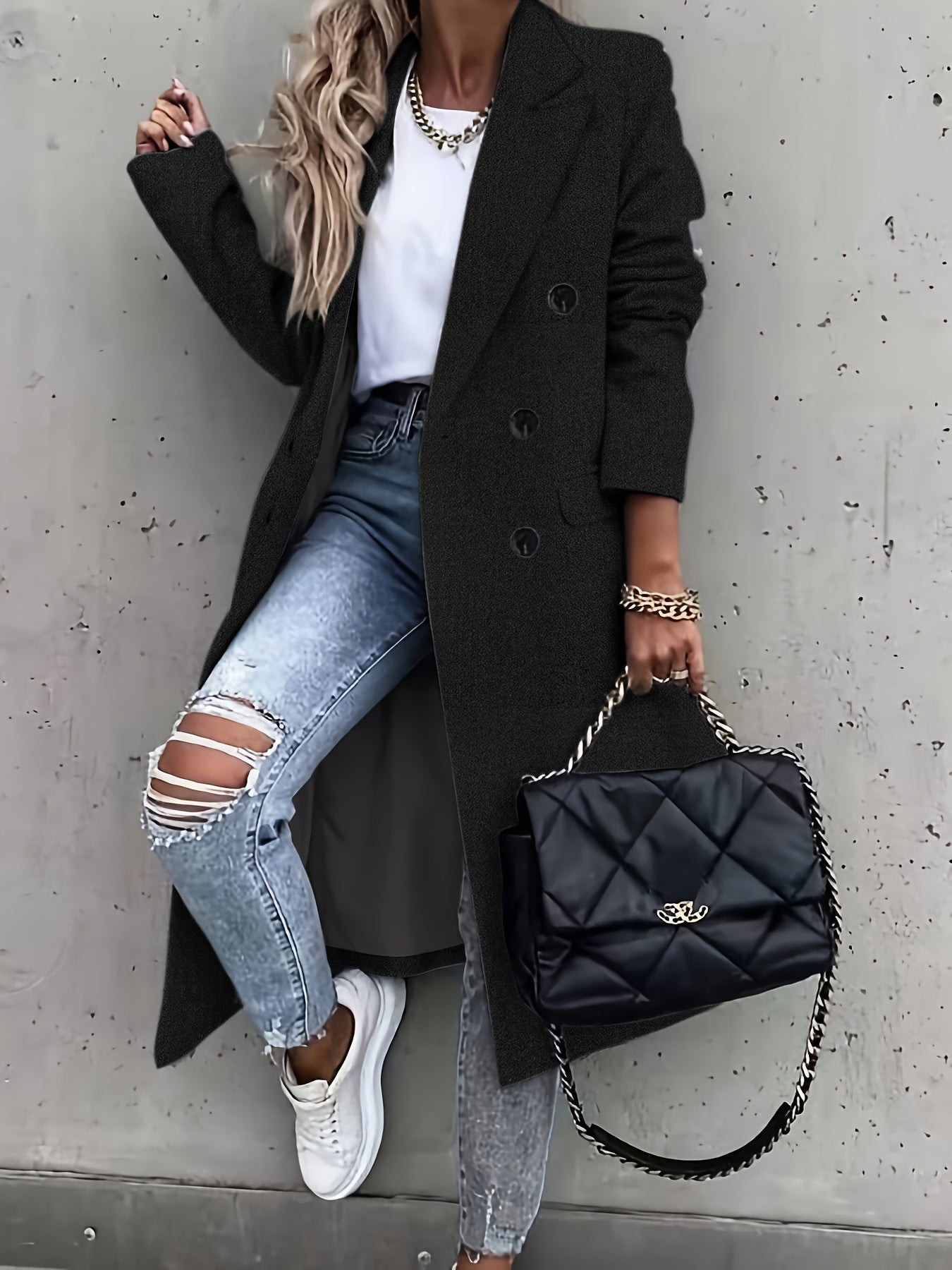 Eleganter schwarzer Mantel, kombiniert mit zerrissenen Jeans und weißem T-Shirt. Modische Handtasche und Sneakers runden den urbanen Look ab.