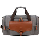 Graue Reisetasche aus Segeltuch mit braunen Lederakzenten, ideal für Wochenendausflüge.