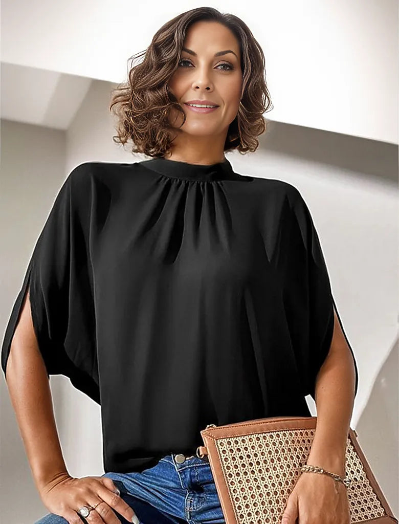 Elegante Frau in schwarzer Bluse mit Fledermausärmeln, hält eine stilvolle Rattan-Clutch. Mode, Damenbekleidung, Accessoires, trendiger Look.
