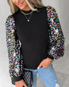 Schwarzes Damenoberteil mit glitzernden Paillettenärmeln, kombiniert mit blauer Jeans. Perfekt für modische, festliche Anlässe.