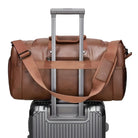 Braune Ledertasche auf silbernem Rollkoffer, Reisegepäck, stilvoll, robust, verstellbarer Schultergurt.