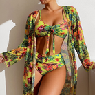 Frau in gelbem Blumen-Bikini mit passender Mesh-Bluse, hoch tailliert, tropisches Design.