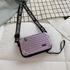 Lila Mini-Koffer Handtasche mit "Forever Young" Gurt auf kariertem Hintergrund.