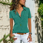 Frau in grüner Bluse und weißer Hose vor Steinmauer, Sommermode, Freizeitkleidung.