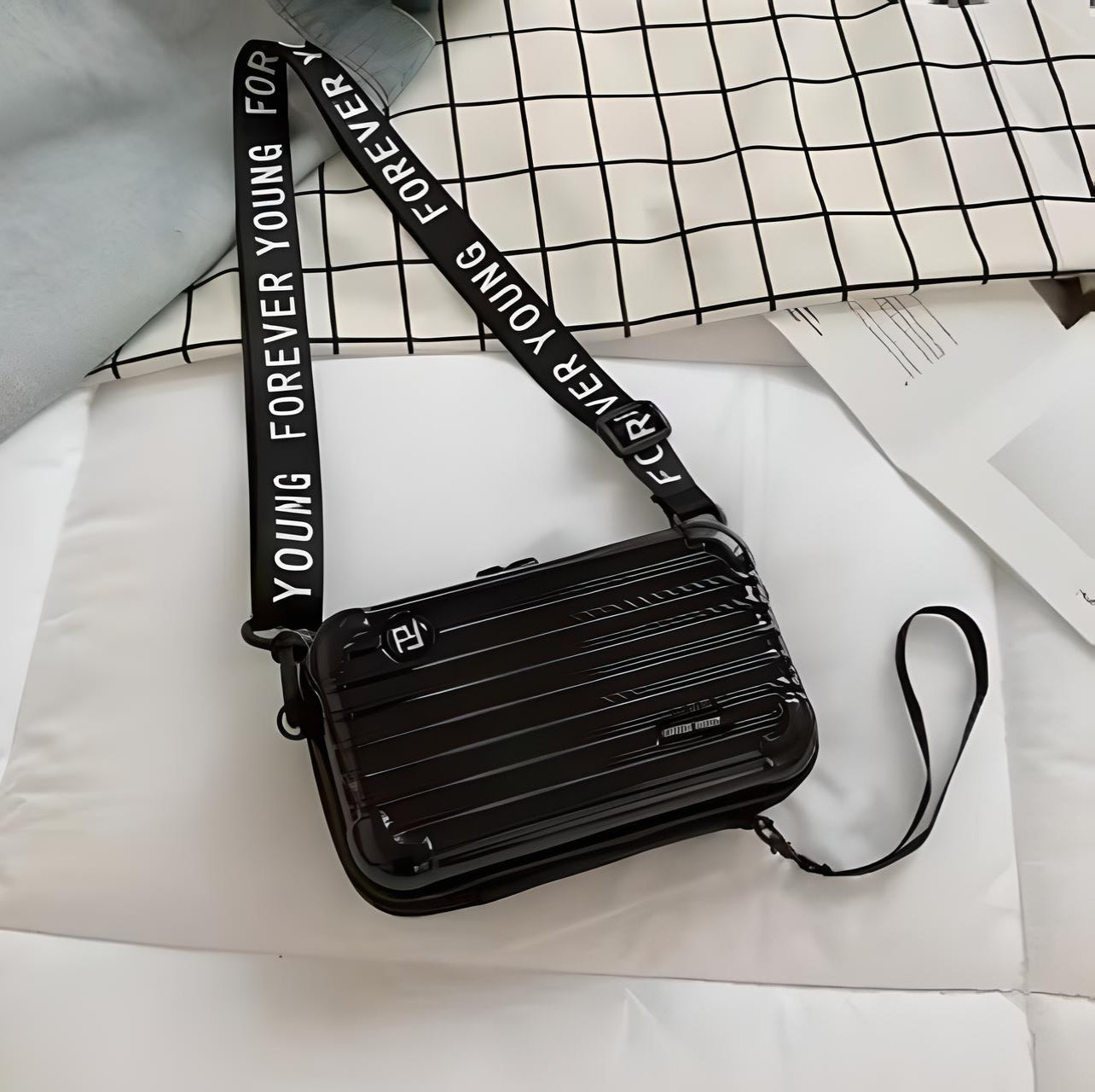 Schwarze Umhängetasche mit Schriftzug "Forever Young", modernes Design, auf kariertem Hintergrund.