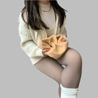 Frau in beiger Strickjacke und weißem Rollkragenpullover, hält ein weiches, beiges Accessoire. Modetrend, Herbstmode, Strickmode.