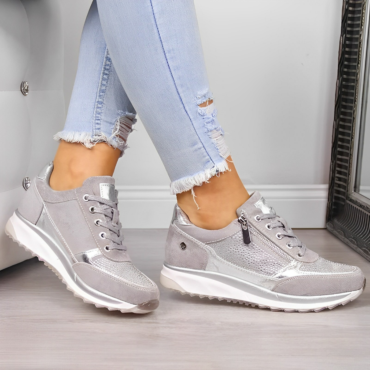 Graue Damen-Sneaker mit Metallic-Details, kombiniert mit hellblauen, zerrissenen Jeans. Modische, bequeme Schuhe für Freizeit und Alltag.