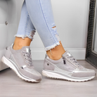 Graue Damen-Sneaker mit Metallic-Details, kombiniert mit hellblauen, zerrissenen Jeans. Modische, bequeme Schuhe für Freizeit und Alltag.