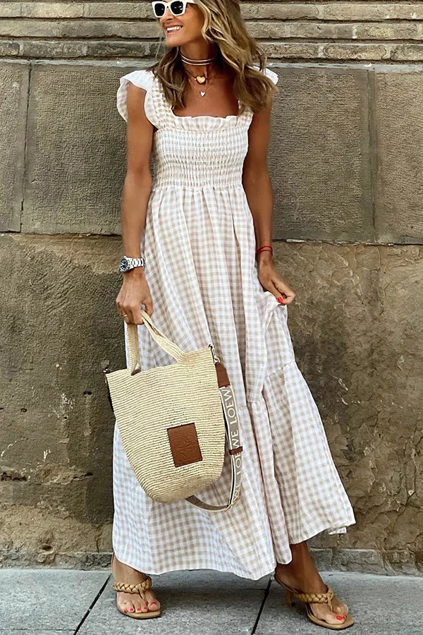 Frau in kariertem Sommerkleid mit Strohtasche, Sonnenbrille und Sandalen. Perfekter Look für Strandmode und Sommeroutfits.