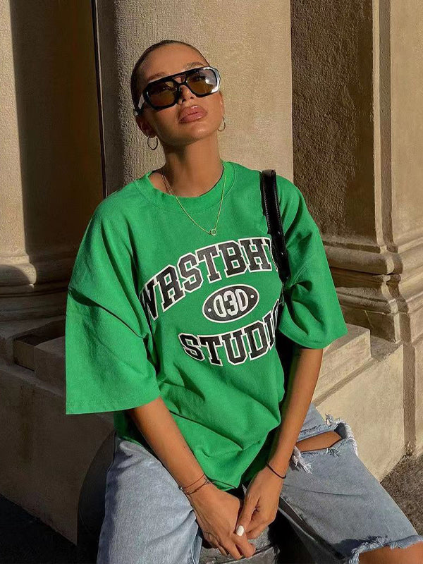 Frau in grünem Oversize-T-Shirt mit "Wastberg Studio"-Aufdruck, Sonnenbrille und zerrissenen Jeans. Streetwear, urbaner Stil, Mode 2023.