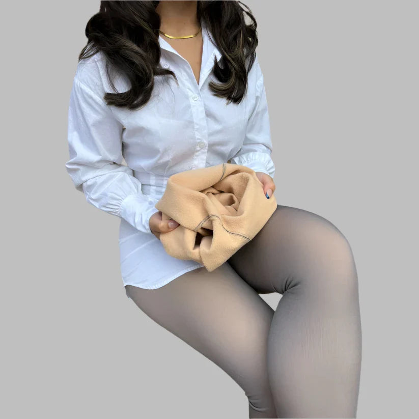 Frau in weißer Bluse und grauer Leggings hält beiges Kleidungsstück. Mode, Damenbekleidung, stilvolle Outfits, Freizeitlook.