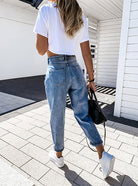 Frau in lässiger Jeans und weißem Crop-Top, trägt schwarze Tasche und weiße Sneaker. Perfekter Streetstyle-Look für den Sommer.