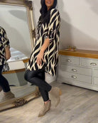 Damenmode: Schwarz-weißes Tunika-Kleid mit abstraktem Muster, kombiniert mit schwarzen Leggings und beigen Stiefeletten. Eleganter Look.