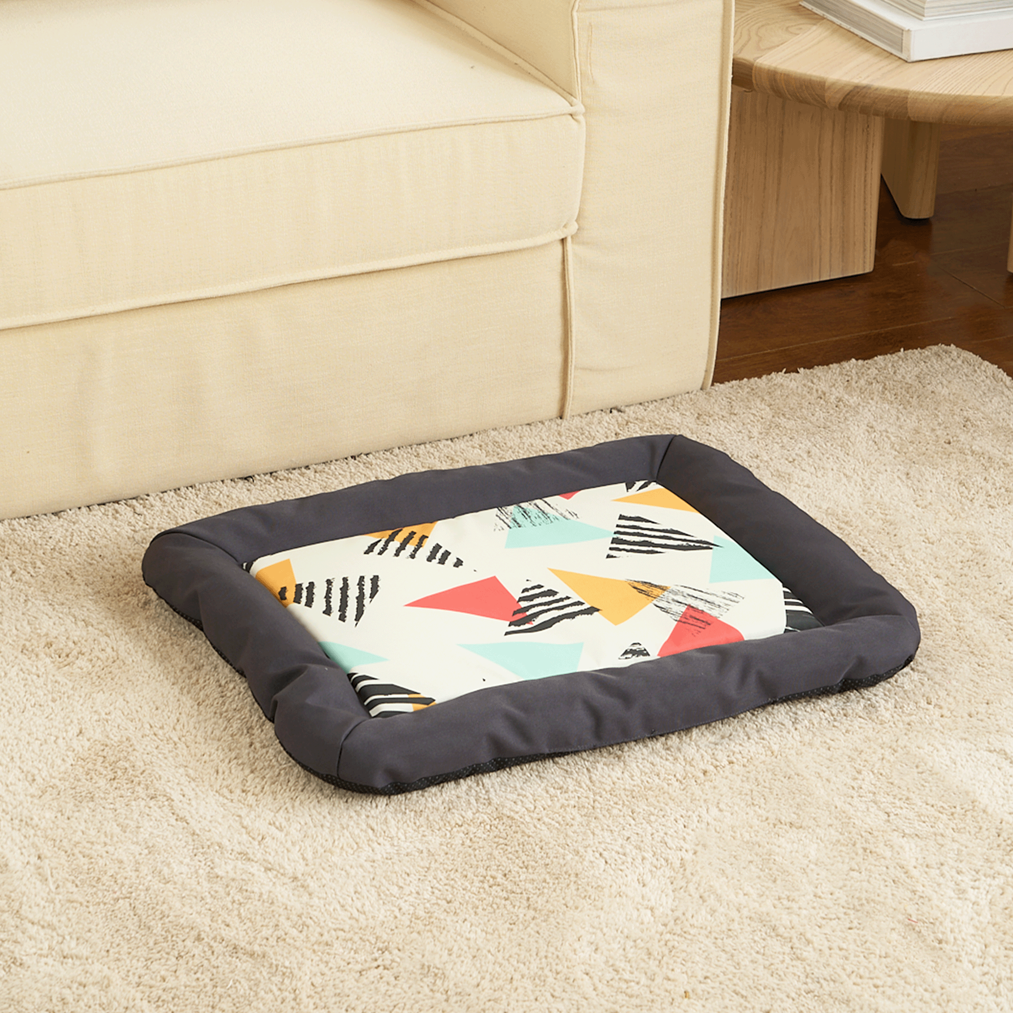 Bunte Hundematte mit geometrischem Muster auf beigem Teppich vor einem Sofa.