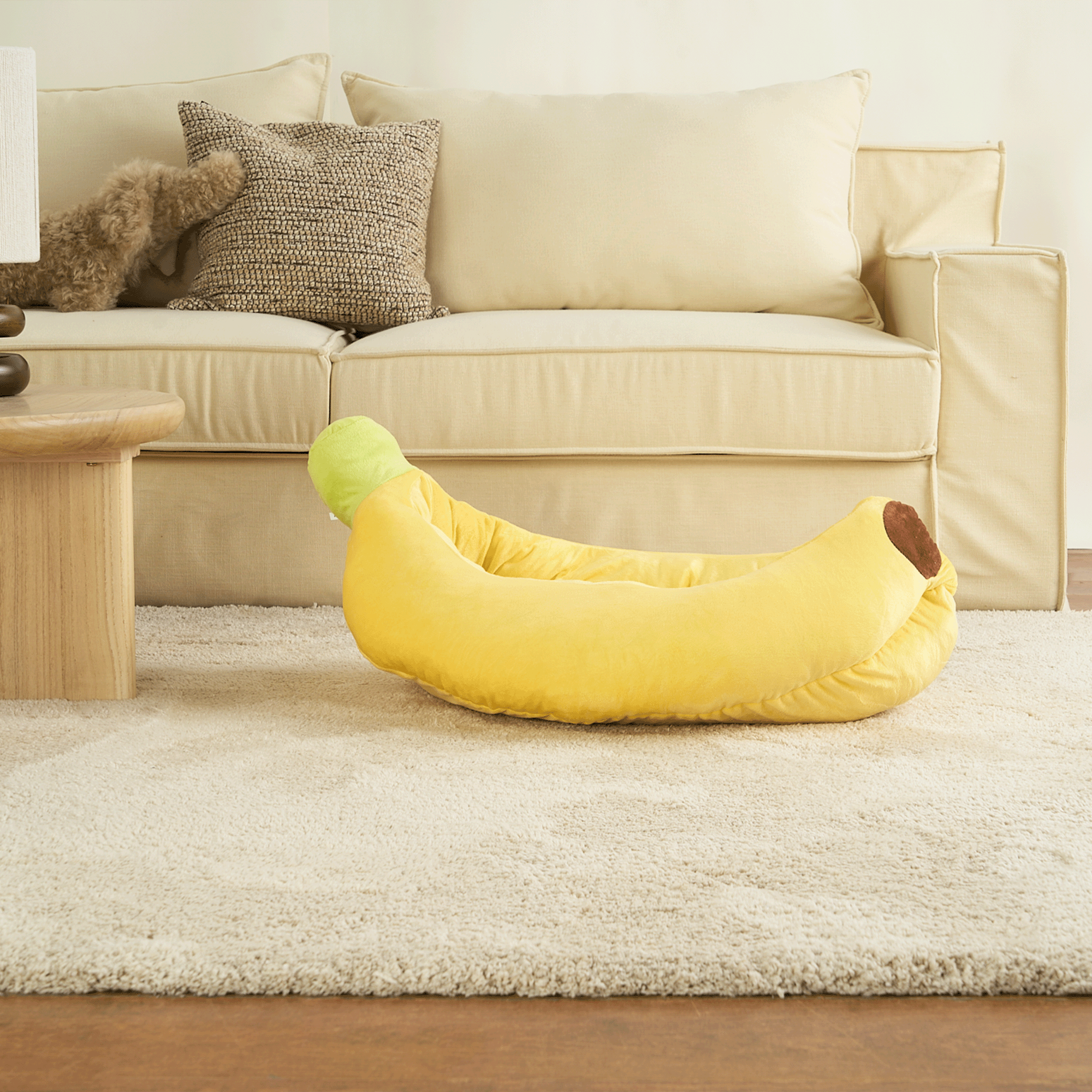 Gelbes Bananen-Sofa-Haustierbett auf beigem Teppich vor cremefarbenem Sofa im Wohnzimmer.