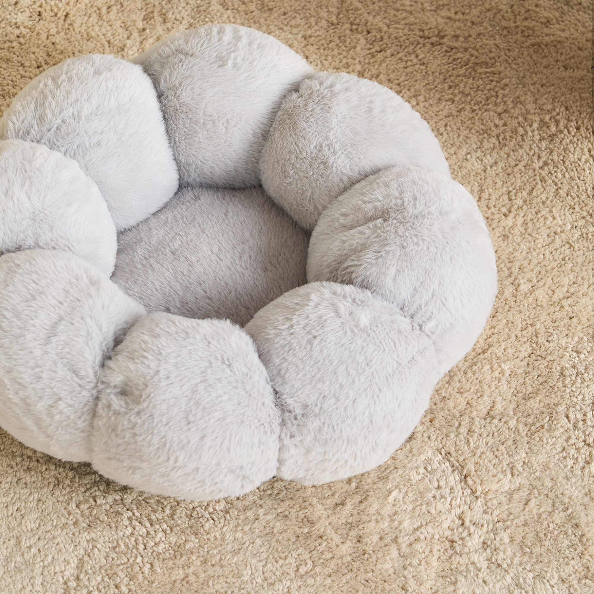 Graues, flauschiges Katzenbett, rund, auf beigem Teppich, ideal für Haustierkomfort.