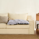 Beige Sofa mit grauer, flauschiger Haustiermatte, gemütliches Wohnzimmer, modernes Design.