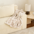 Kuscheldecke aus Kunstfell in Beige auf cremefarbenem Sofa, ideal für Haustiere.