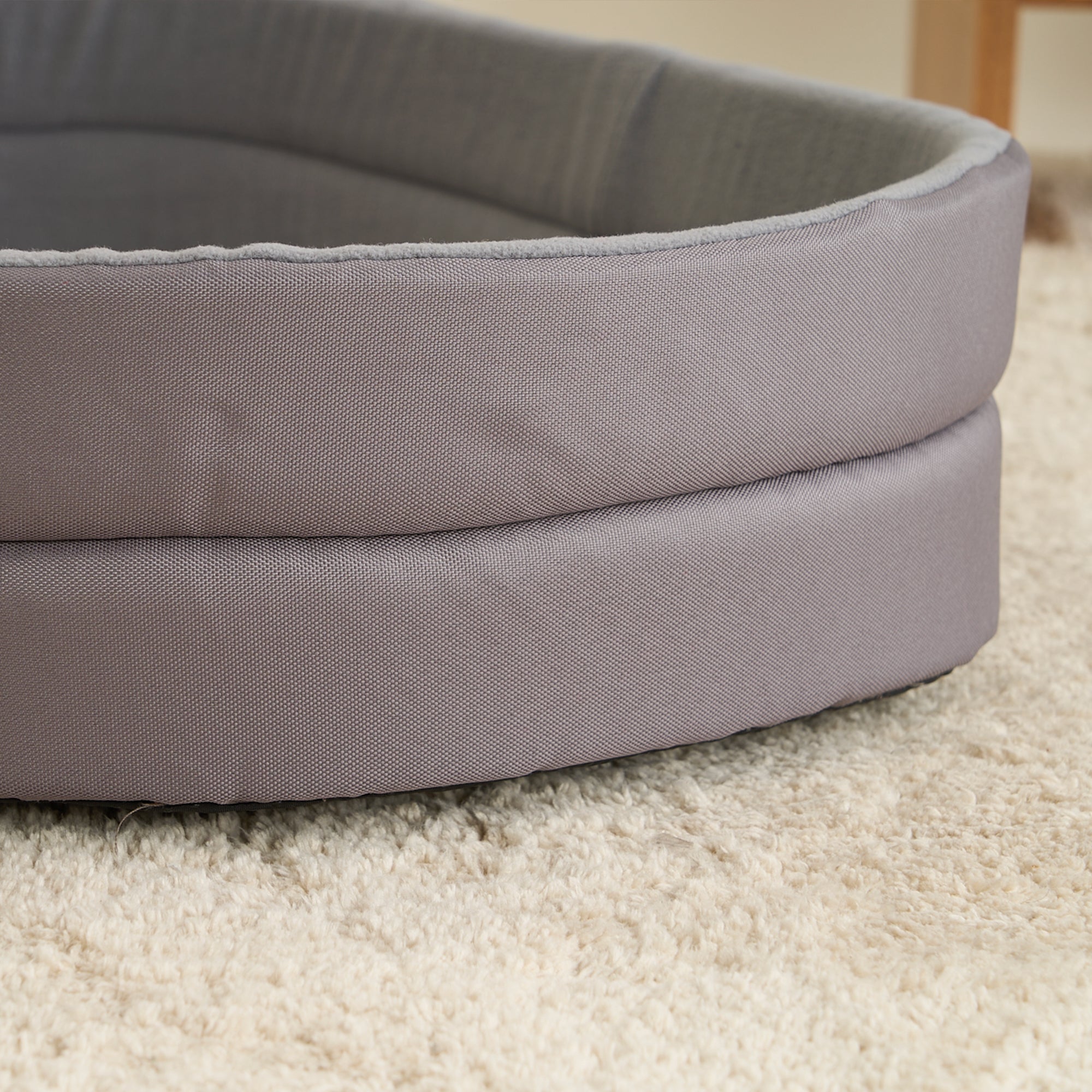 Graues Hundebett aus Stoff auf Teppich, rund und gepolstert, ideal für Haustiere.
