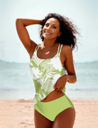 Frau im grünen Tankini mit Blumenmuster am Strand, lächelnd. Sommermode, Bademode, Strandoutfit, stilvoller Badeanzug, Urlaubskleidung.