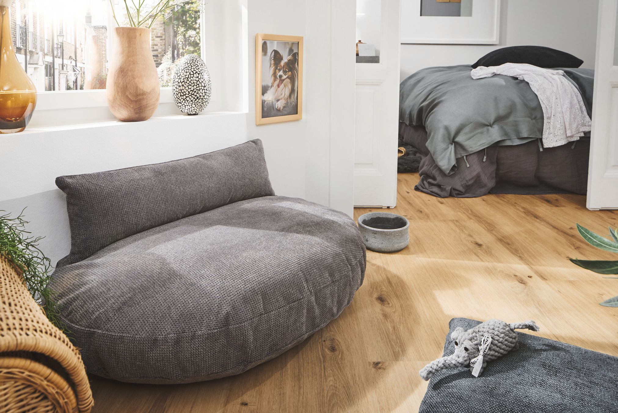 Graues Hundebett aus Stoff im modernen Wohnzimmer, Holzboden, Dekoration, gemütlich.