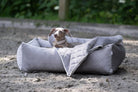 Hund in grauem, gestepptem Hundebett im Freien, komfortabel und stilvoll.