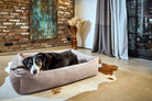 Schwarzer Hund auf grauem Hundebett in modernem Wohnzimmer mit Backsteinwand und Kunstwerk.