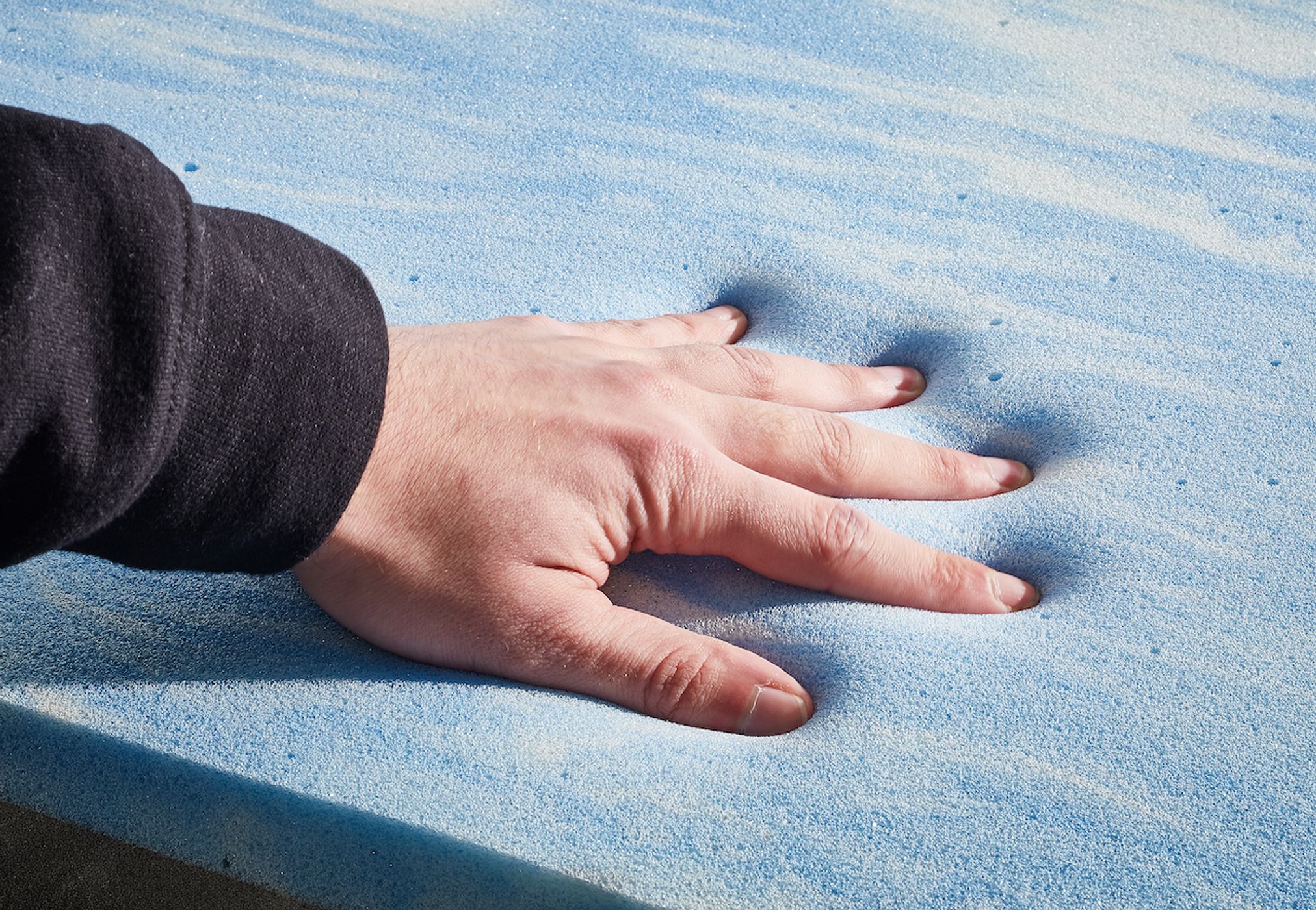 Hand drückt auf blauen Memory-Schaumstoff, Matratze, Komfort, Druckentlastung, Nahaufnahme.